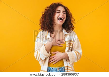 Image of cheerful woman 20s with curly hair standing and laughing, isolated over yellow background