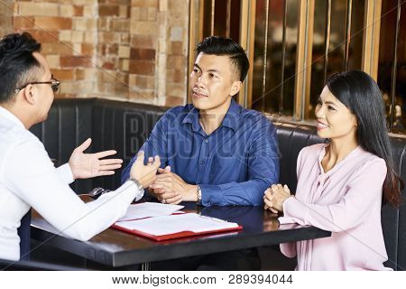 Vietnamese Couple Listening To Real Estate Agent During Meting In Cafe