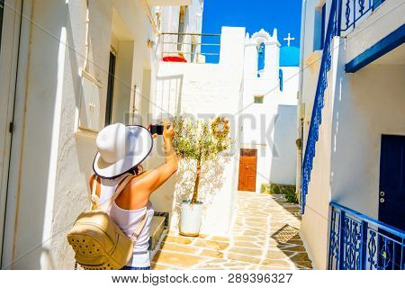 Girl in a white hat taking photo of cute green windows on the slope of sunshine greek street