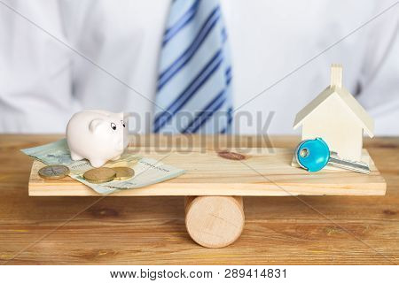 Saving For A House And Balance Concept With Money And Piggy Bank On A Swing
