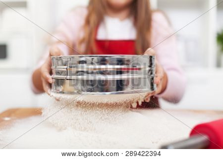 Young girl hands sifting flour with a metallic sieve in the kitchen - close up, shallow depth