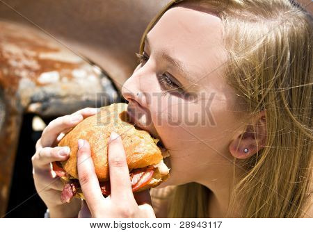Jeune femme de croquer dans un très gros pain maison rempli de tomates et bacon