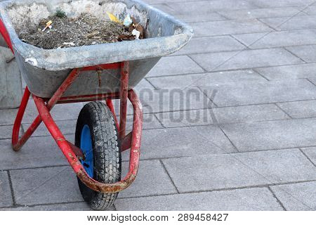Wheelbarrow With Trash On The Pavement, Street Cleaning. Trash Removal In City, Urban Landscaping In