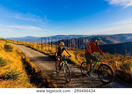 Cycling woman and men riding on bikes at sunset mountains forest landscape. Couple cycling MTB enduro flow trail track. Outdoor sport activity.