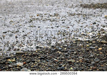 Pebbles On A Sandy Beach, Shiny Wet Stones And Waves.