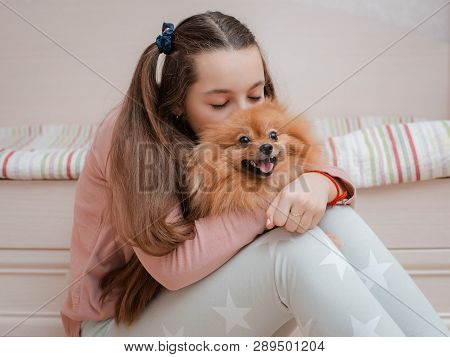 Teenage Girl With A Dog Breed Spitz Rejoices With A Pet At Home On The Floor. Care And Training Of A