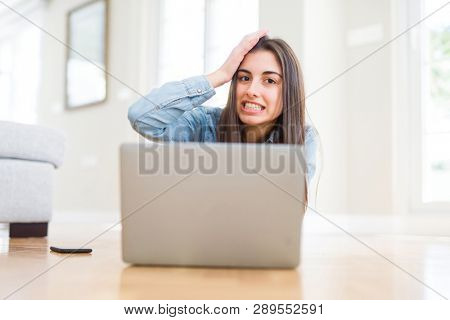 Beautiful young woman laying on the floor using laptop stressed with hand on head, shocked with shame and surprise face, angry and frustrated. Fear and upset for mistake.