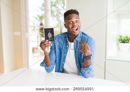 African american man holding passport of Canada with surprise face pointing finger to himself