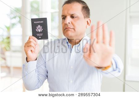 Middle age man holding holding passport of United States with open hand doing stop sign with serious and confident expression, defense gesture