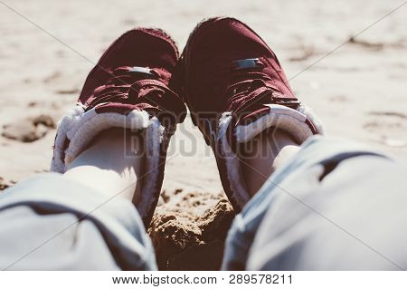 Feet Of Young Woman In Sport Footwear And Jeans Relaxing After Hiking On Sand Beach. Pov. Adventure 