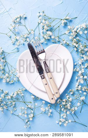 Plates In Form Of Hearts, Knife And Fork And  Fresh White Gypsofila  Flowers On Blue Textured Backgr