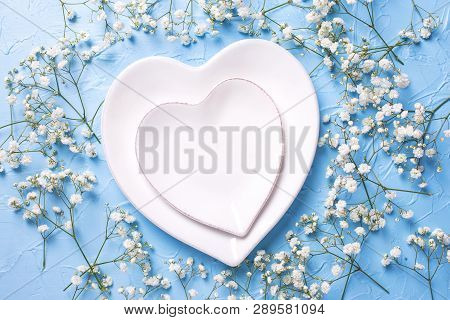 Plates In Form Of Hearts And  Fresh White Gypsofila  Flowers On Blue Textured Background. Top View. 