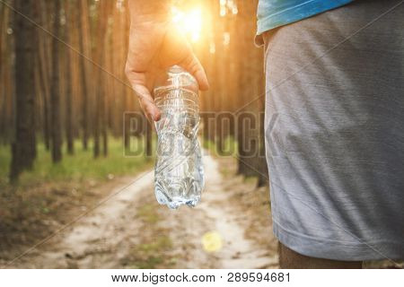Man Holding A Bottle Of Water On The Background Of A Dirt Road In The Woods. Concept Of Training In 