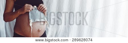 Close Up View Of Nacked Belly Of Pregnant Woman Holding Baby Boy Hat. Pregnant Woman Is Holding A Sm