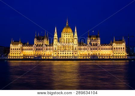 Illuminated Budapest Parliament Building At Night With Dark Sky And Reflection In Danube River, Hung