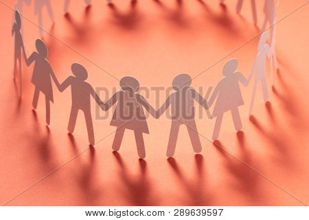 Circle of paper people holding hands on pink surface. Community, union concept. Society and support.