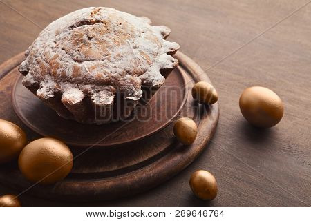 Easter Yeast Cake Sprinkled With Powdered Sugar And Golden Eggs On Wooden Table
