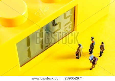 Yellow Alarm Clock With At Eleventh Hour Time With Little Miniature Figurines Standing In Front Of T