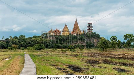 Rice Field With Wooden Boardwalk With Wat Tham Suea In The Background