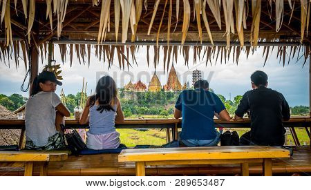 Four People Sitting On Cafe Bench Looking At Wat Tham Suea
