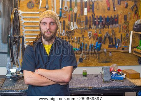 Blue Eyed Beraded Guy In Black Shirt And Yellow Hat In The Workshop