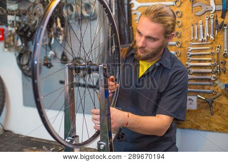 Blue Eyed Beraded Guy In Black Shirt Repairing Bicycle In The Workshop