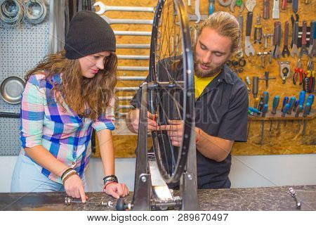 Handsome Beraded Guy And The Pretty Girl Repairing Bicycle In The Workshop Together