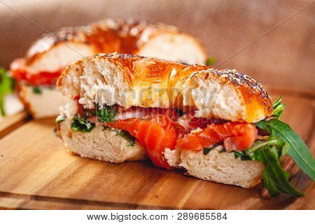 Bagel With Cream Cheese, Smoked Salmon And Arugula Salad Cut In Half On Wooden Board. Close Up