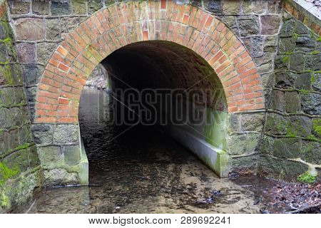 Stone Culvert Over The Road For A Small River. A Small Stream In A Forest Area. Season Of The Spring