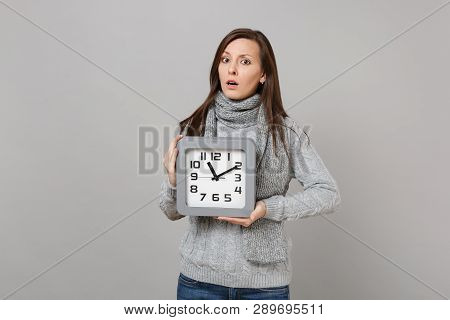 Puzzled Young Woman In Gray Sweater, Scarf Hold Square Clock Isolated On Grey Background, Studio Por