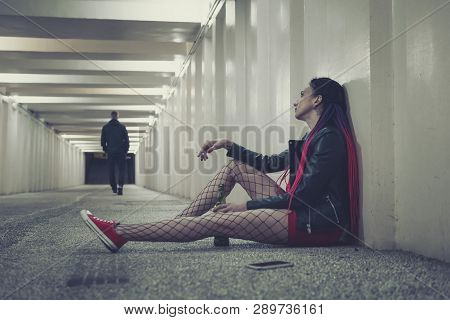Girl Sitting On The Floor In The Tunnel With A Bottle Of Whiskey And Looks At The Outgoing Of A Guy 