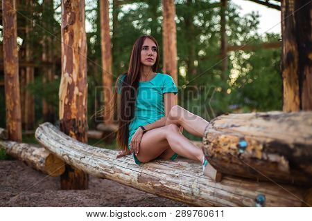 Girl In Turquoise Short Dress Sitting On A Tree Log