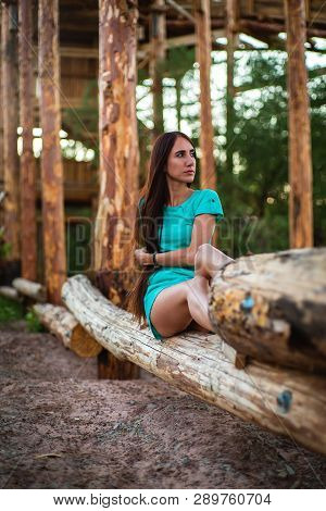 Girl In Turquoise Short Dress Sitting On A Tree Log