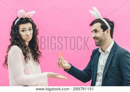 Young Happy Couple On The Pink Background. On The Head Is A Rabbit Ears. A Young Man Holding A Small