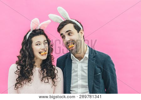 Young Happy Couple Standing On Pink Background. On The Head Of The Ears Of The Bunny. During This Ma