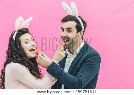 Young Happy Couple Standing On Pink Background. On The Head Of The Ears Of The Bunny. During This Ma