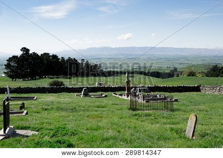 View Across Old Cemetery With Broken Headstones To Expansive Rural Fields And Distant Hills In Centr