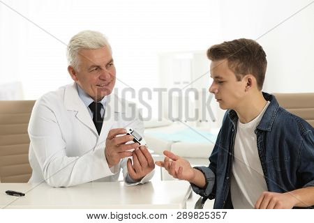 Doctor Checking Patient's Blood Sugar Level With Digital Glucometer At Table. Diabetes Control