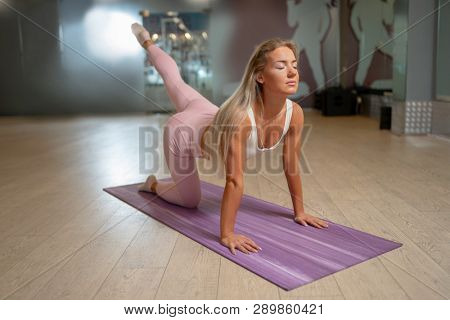 Blonde woman standing on all fours on mat doing yoga.
