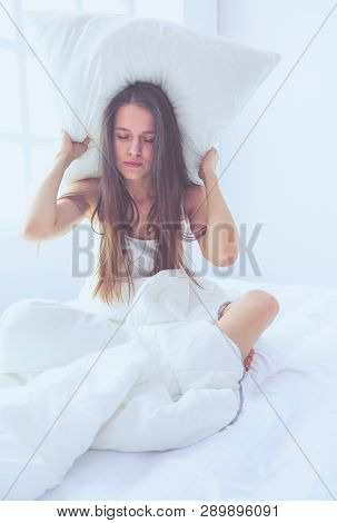 Young caucasian woman covering her head and ears with pillows.