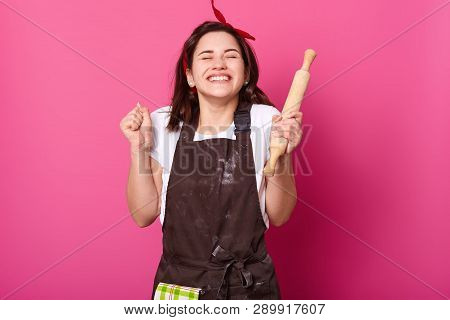 Baker Woman Holds Baking Rolling Pin, Wears Brown Apron, White T Shirt. Young Girl Bends Elbows And 