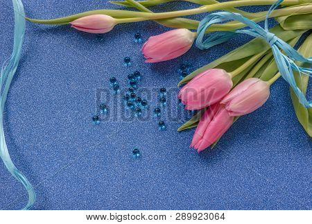 Pink Tulips With Blue Ribbon And Blue Beads On Blue Glitter Background With Copy Space