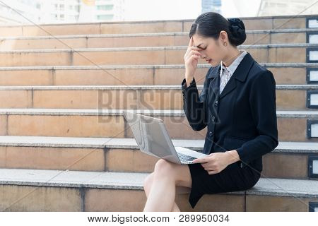 Asian Businesswoman Sit On The Staircase And Looking At Laptop. She Stress And Used Her Hand To Tuch