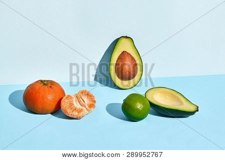 Composition Of Fresh Fruits, Mandarin Lime And Two Halfs Of Cutted Avocado On Two-colored Background