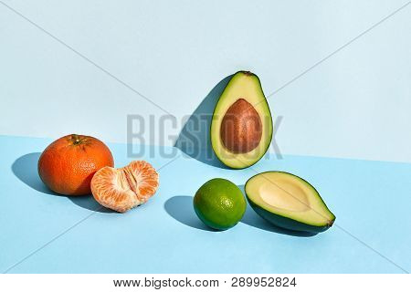 Composition Of Fresh Fruits, Mandarin Lime And Two Halfs Of Cutted Avocado On Two-colored Background