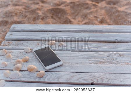 The Smartphone Lies In The Encircling Of Seashells On Wooden Boards.