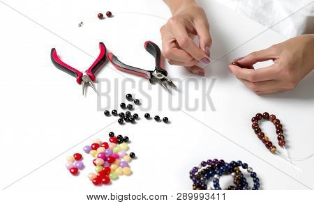 Making Bracelet Of Colorful Beads. Female Hands With A Tool On A White Background. Selective Focus.