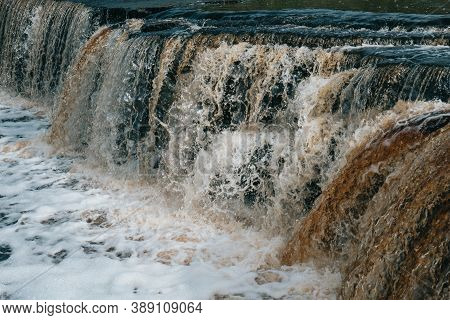 Waterfall, Water Flowing From The River Falls Down. A Stormy River With A Brown Hue.
