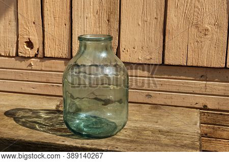 Empty Glass Jar. A Three Liter Jar Stands On A Wooden Bench Near The House.
