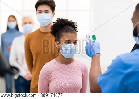 Medical Worker Doing Temperature Screening Measuring Fever For Diverse People Standing In Queue, Usi
